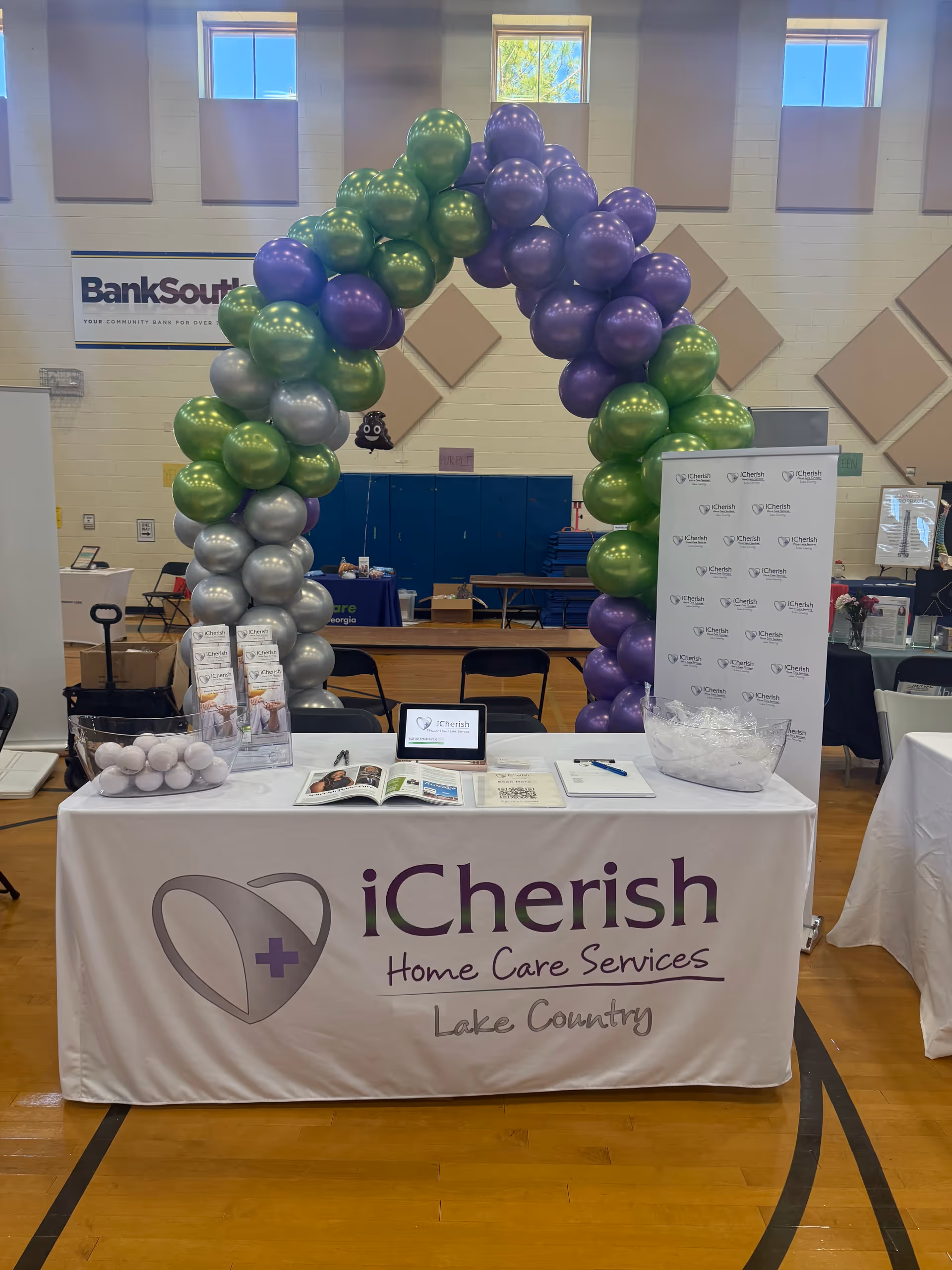 Indoor event booth for iCherish Home Care Services with a purple and green balloon arch.
