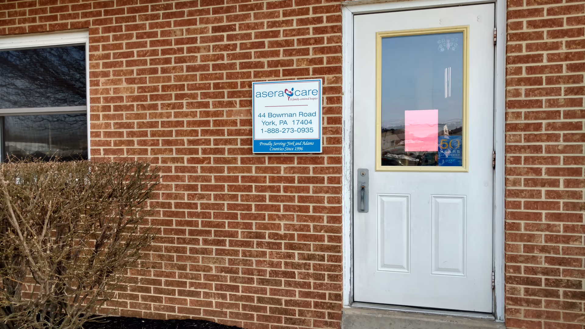 Brick exterior wall with a white entry door and blue hospice care sign.