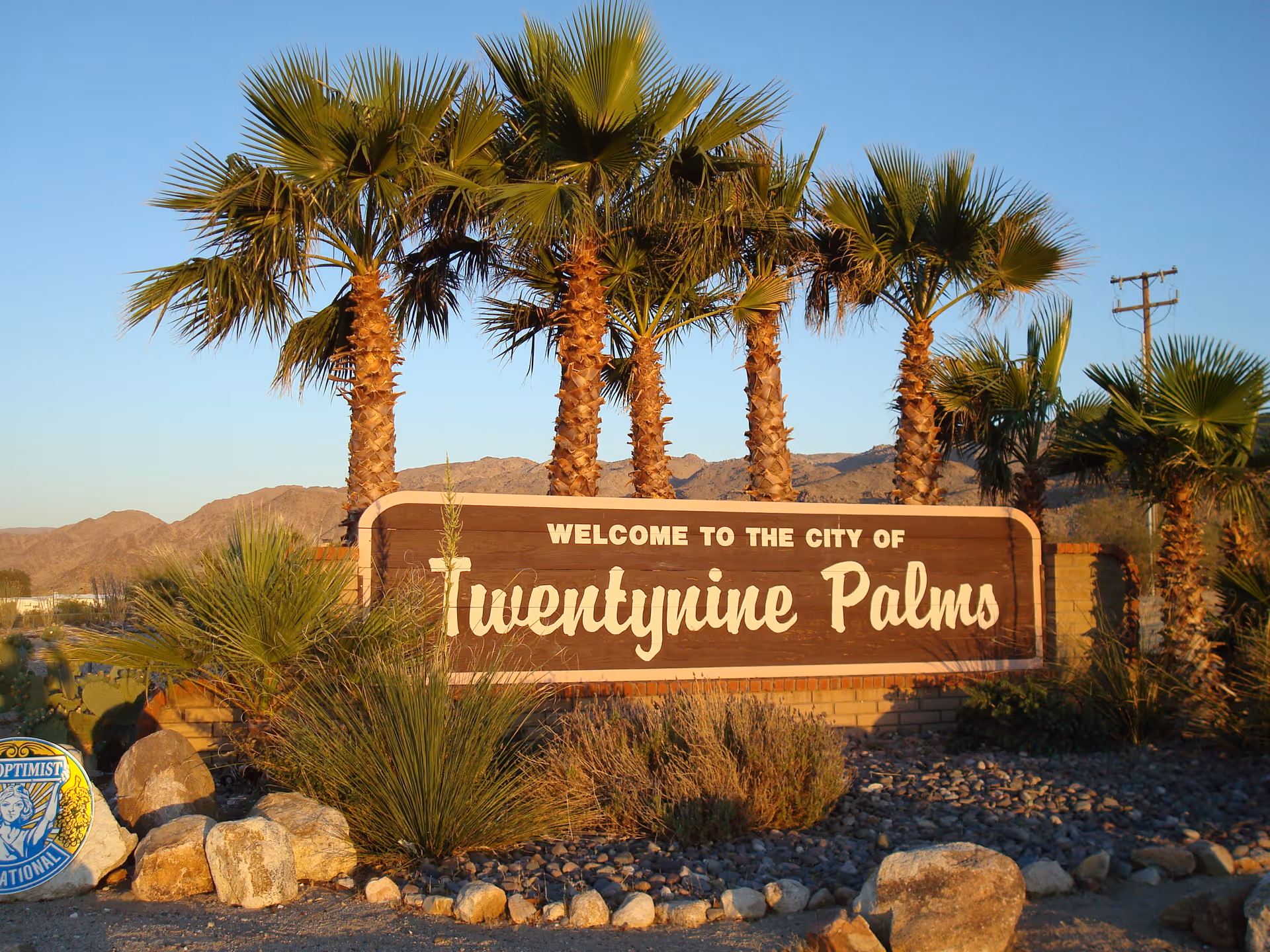 Exterior scene with a welcome sign for Twentynine Palms surrounded by palm trees.