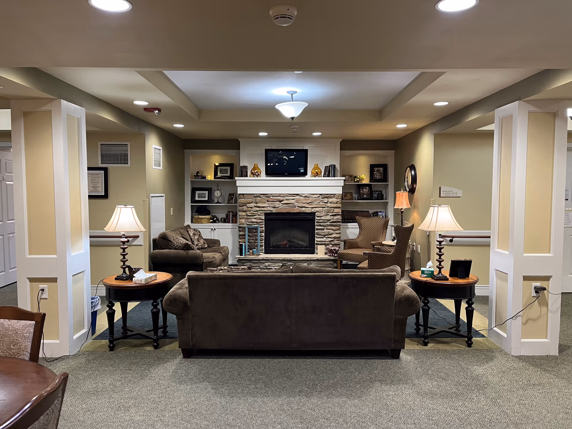 Cozy Augusta Place living room lounge with fireplace, sofas, chairs, lamps, and built-in shelves.