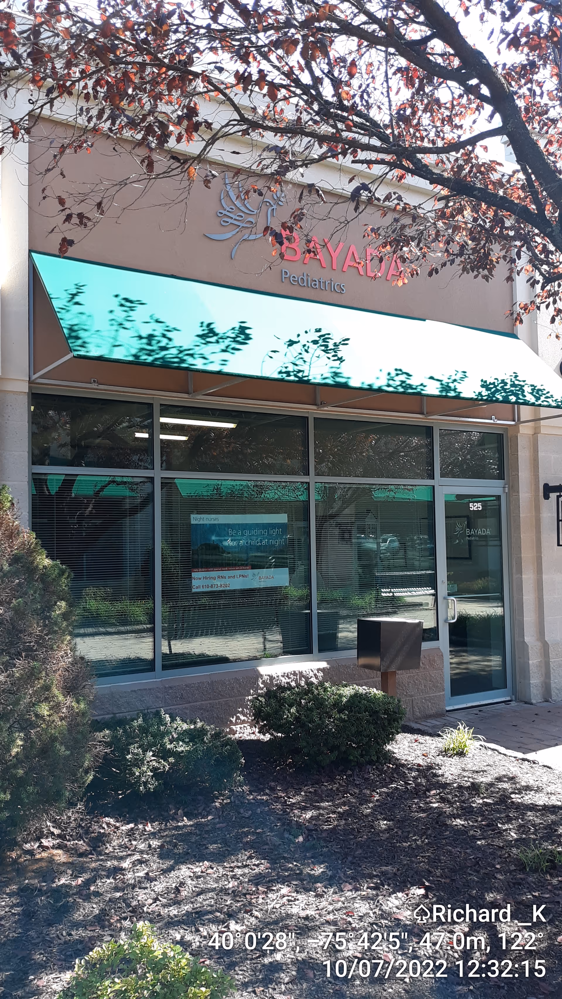 Front exterior of a facility with glass doors, green awning, and landscaping.