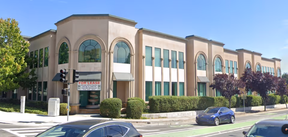 Two-story beige building with arched windows and a 'For Lease' sign.