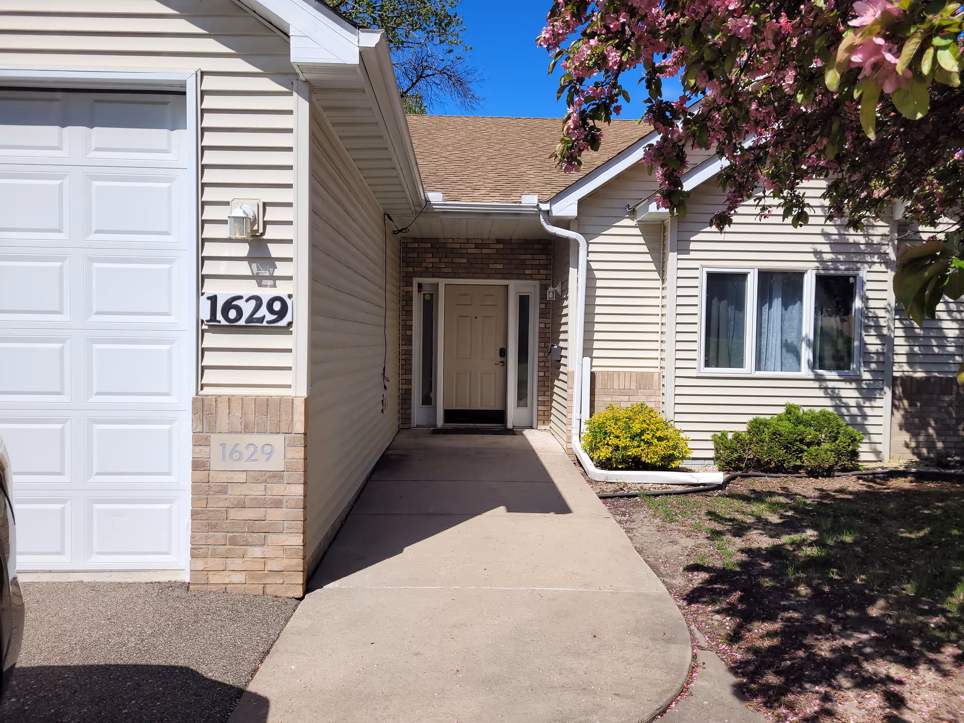 Front view of beige senior living facility entrance with shrubs and a flowering tree