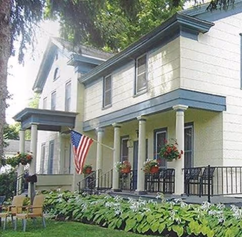 Front exterior of a senior living facility with columns, a porch, and an American flag.