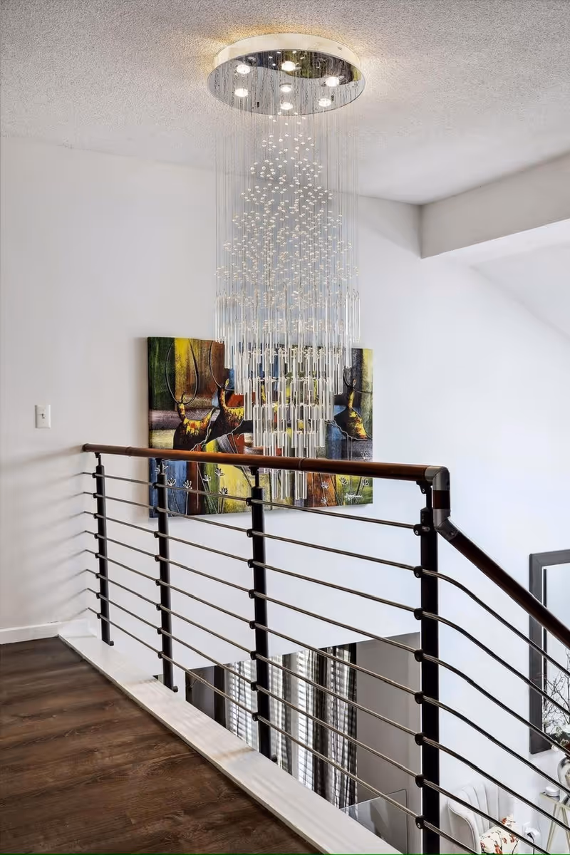 Interior staircase landing with dark metal railing, wooden floor, and cascading crystal chandelier.