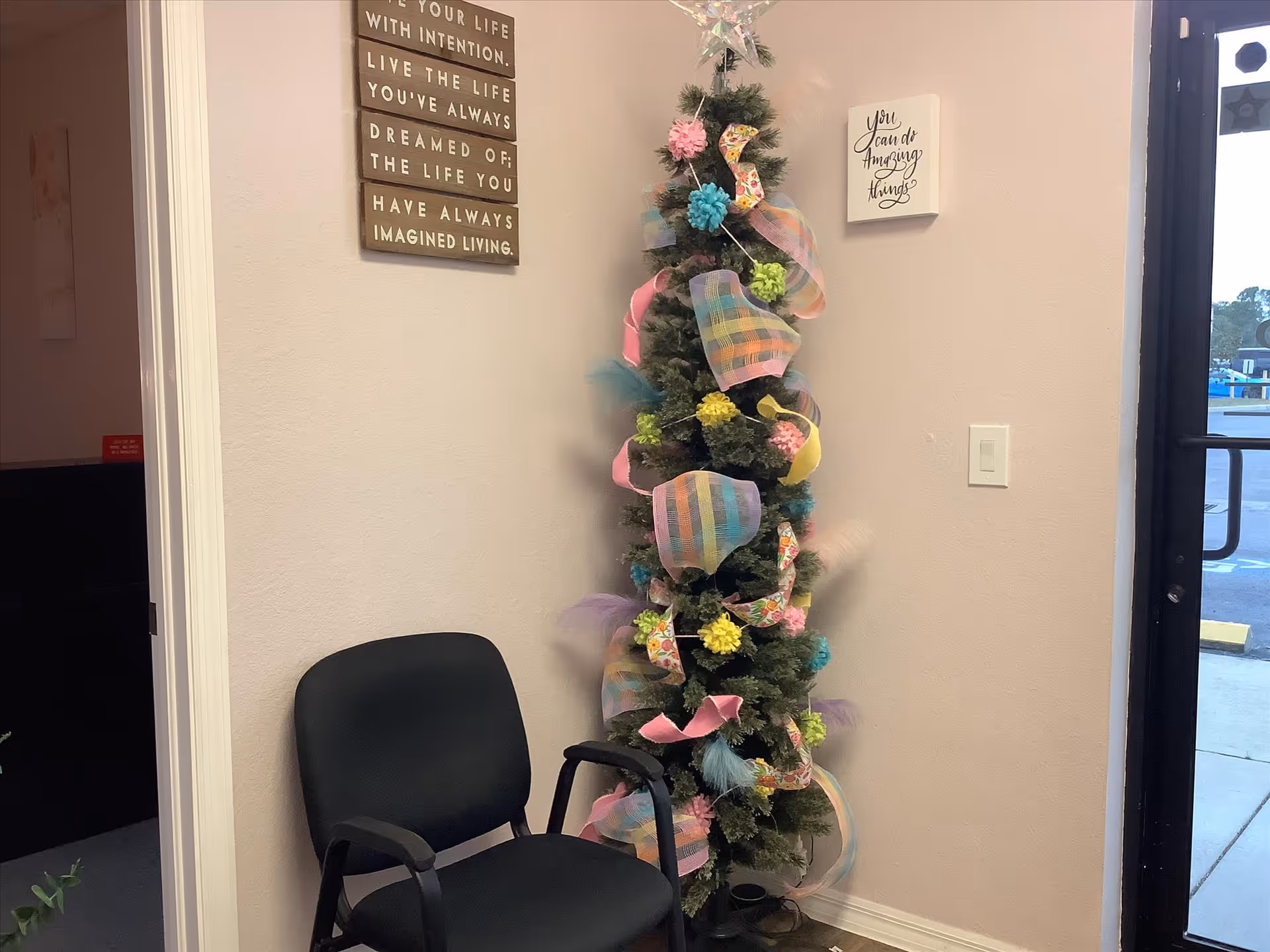A decorated Christmas tree beside a black chair in a pink-walled interior corner.