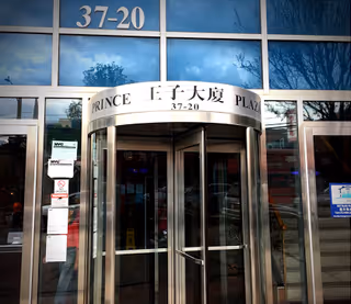 Front entrance of a glass building with a curved metal canopy reading 37-20 Prince Plaza.