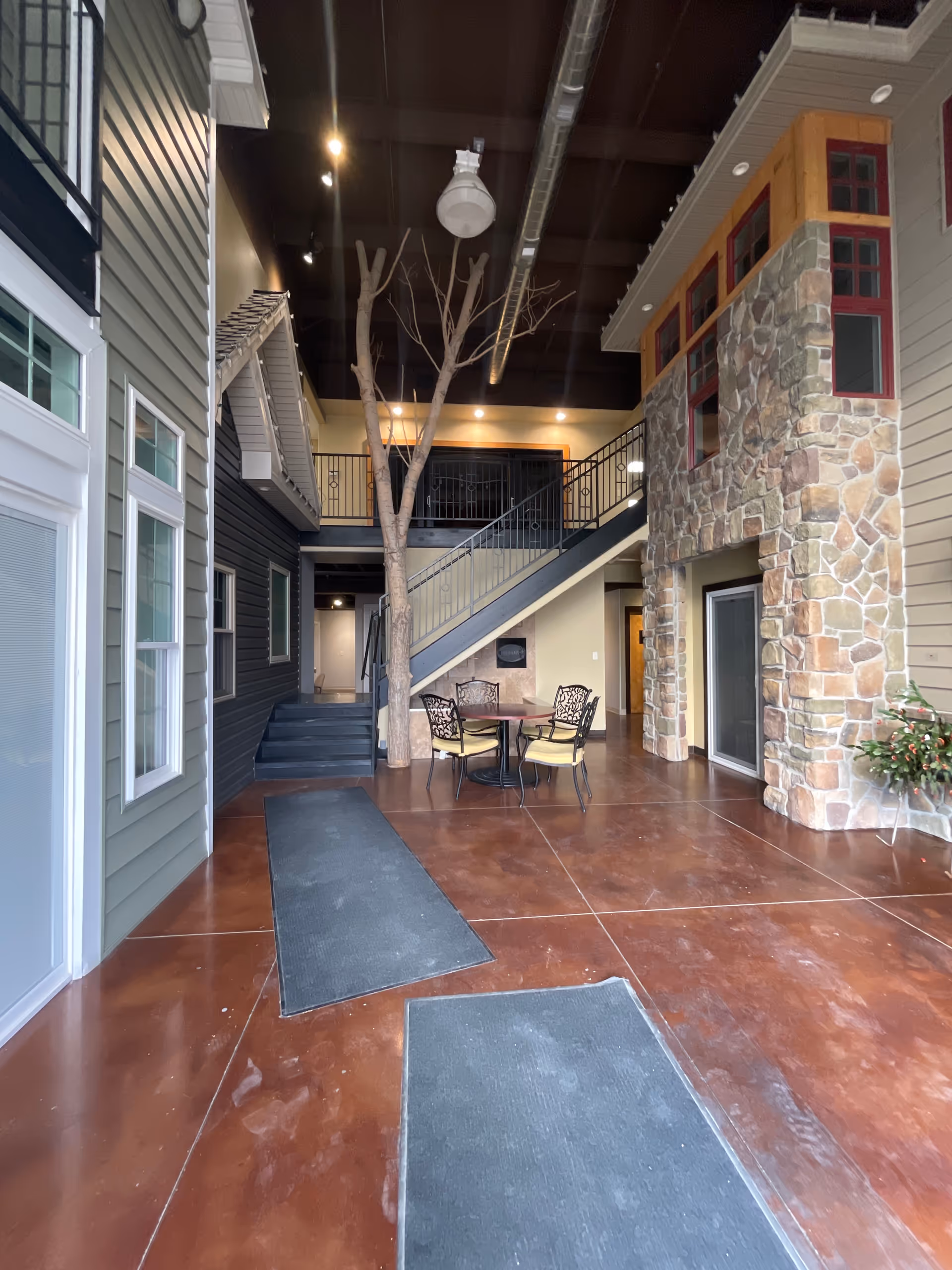 Indoor atrium of a senior living facility with tree, staircase, stone wall, and tables.