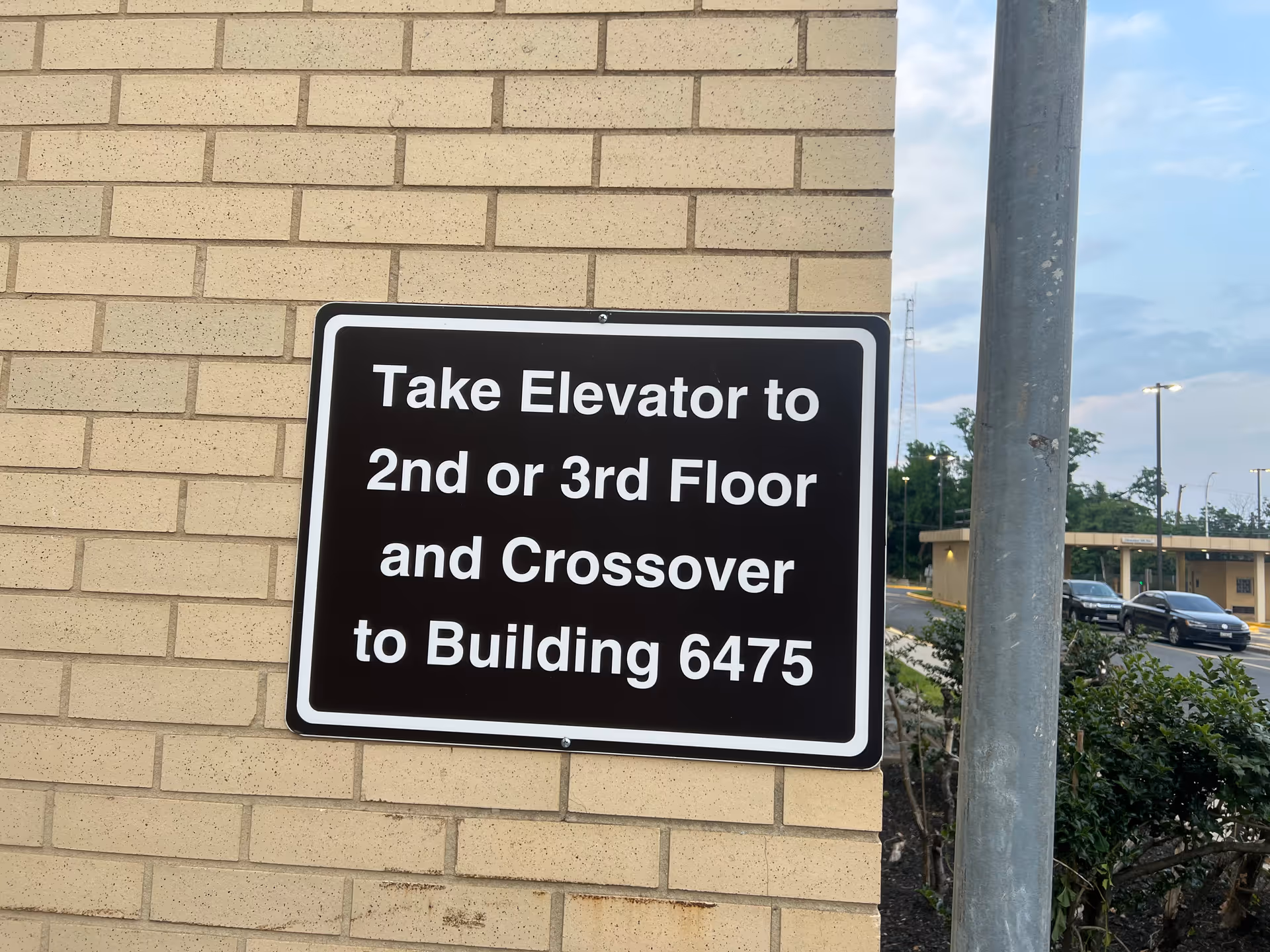 Sign on brick wall directs to elevator for 2nd/3rd floor and crossover to Building 6475.
