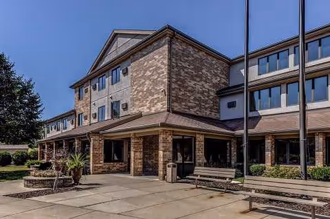 Exterior view of Elizabeth Gardens, a brick senior living facility with entrance, benches, and planters.