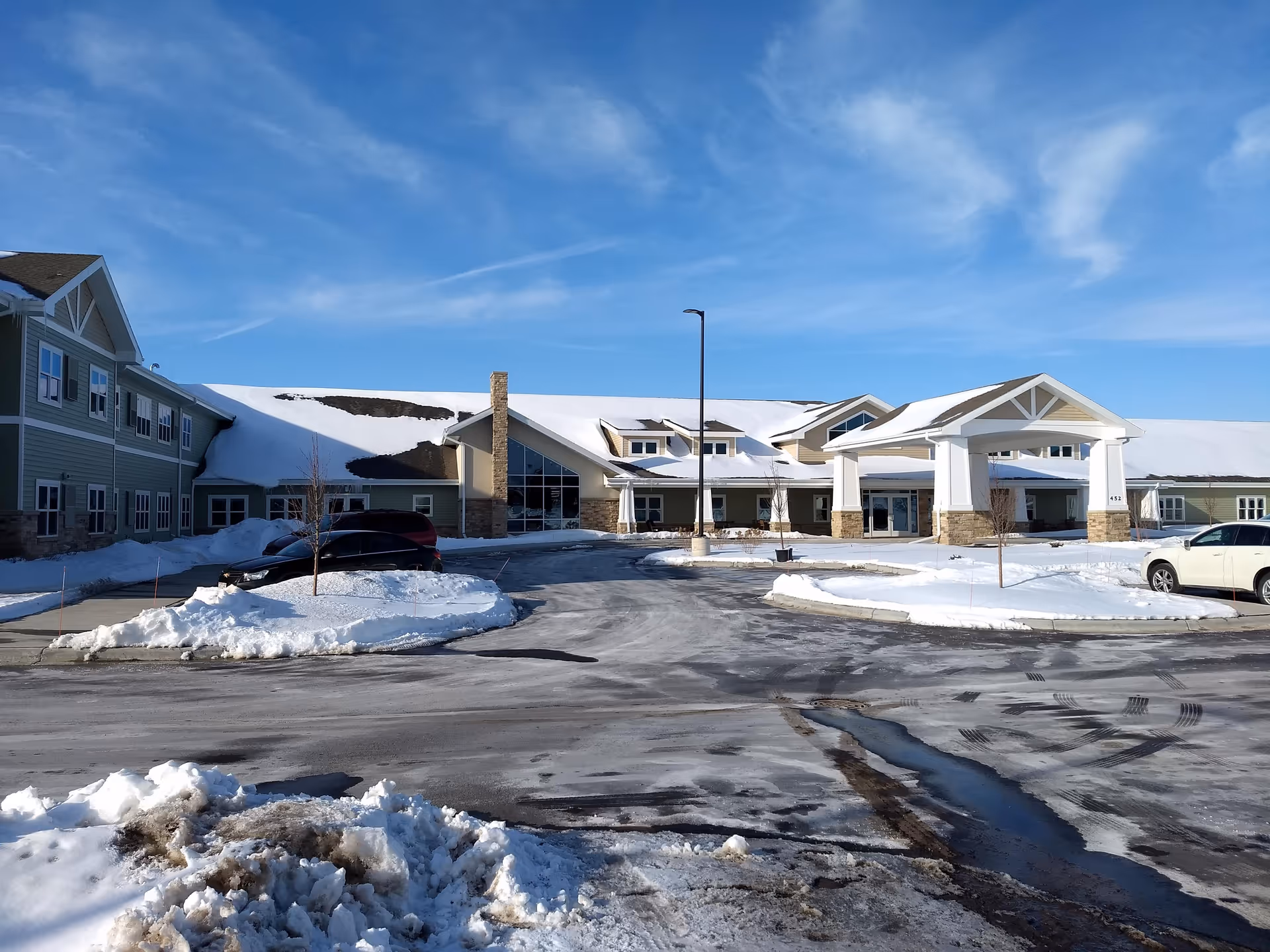 Snow-covered exterior of a senior living facility with a covered entrance and parking.