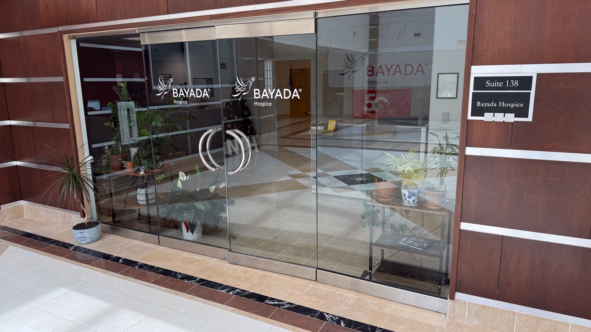 Glass entrance of Bayada Hospice with double doors and potted plants outside.