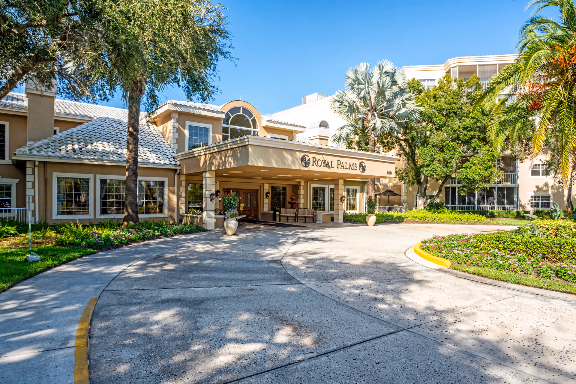Exterior view of Royal Palms senior living entrance with driveway and palm trees.