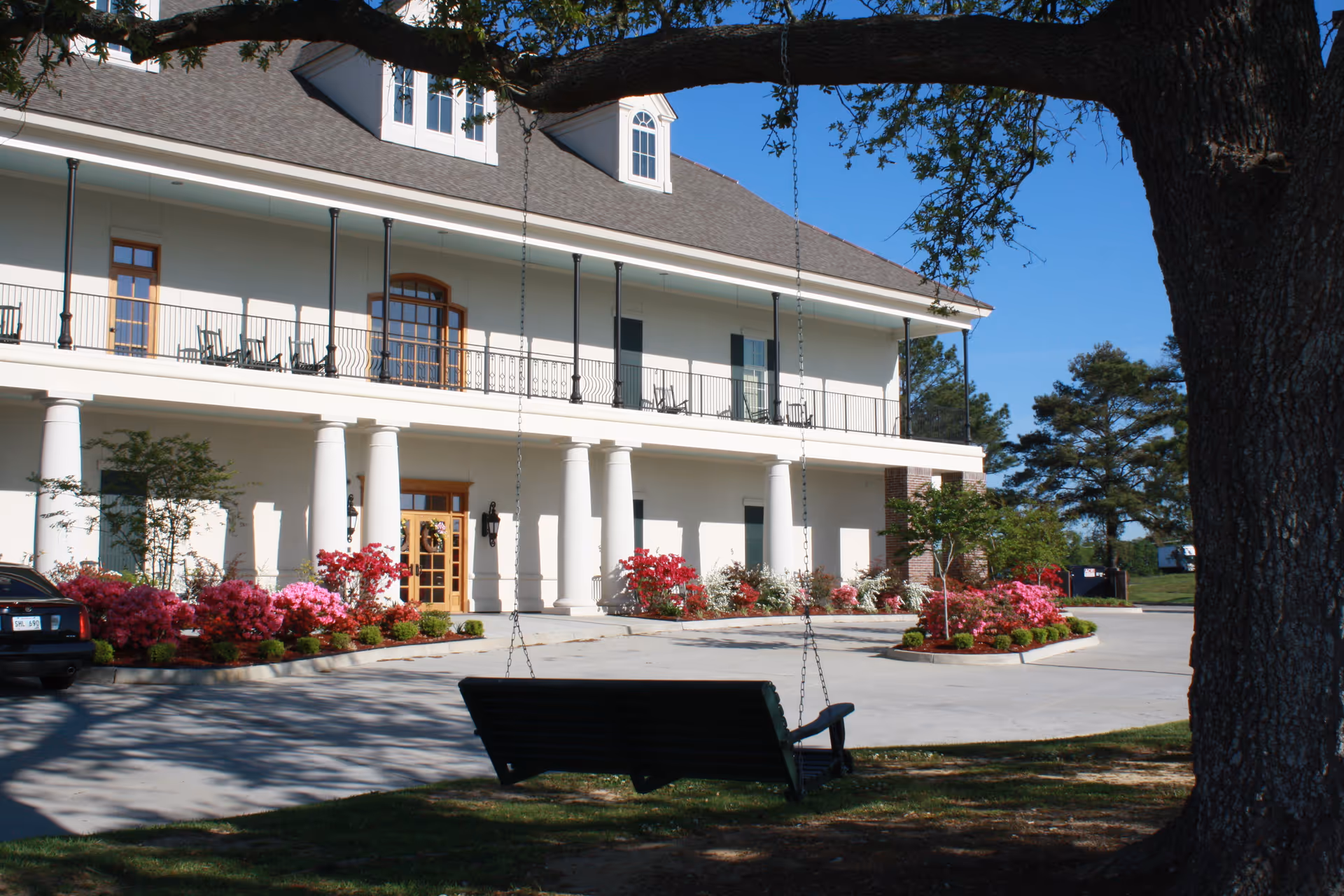 Front view of a two-story senior living facility with columns, flowers, and a porch swing.