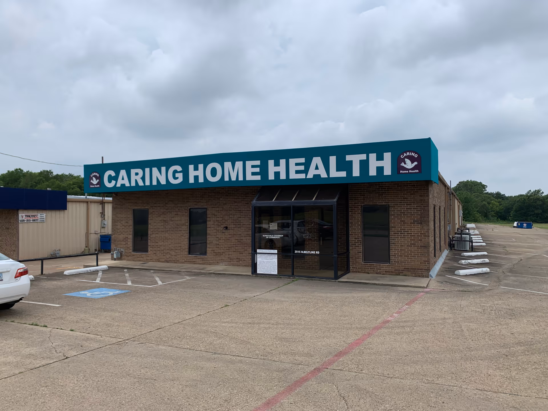 Front view of a brick building with a teal Caring Home Health sign and parking.