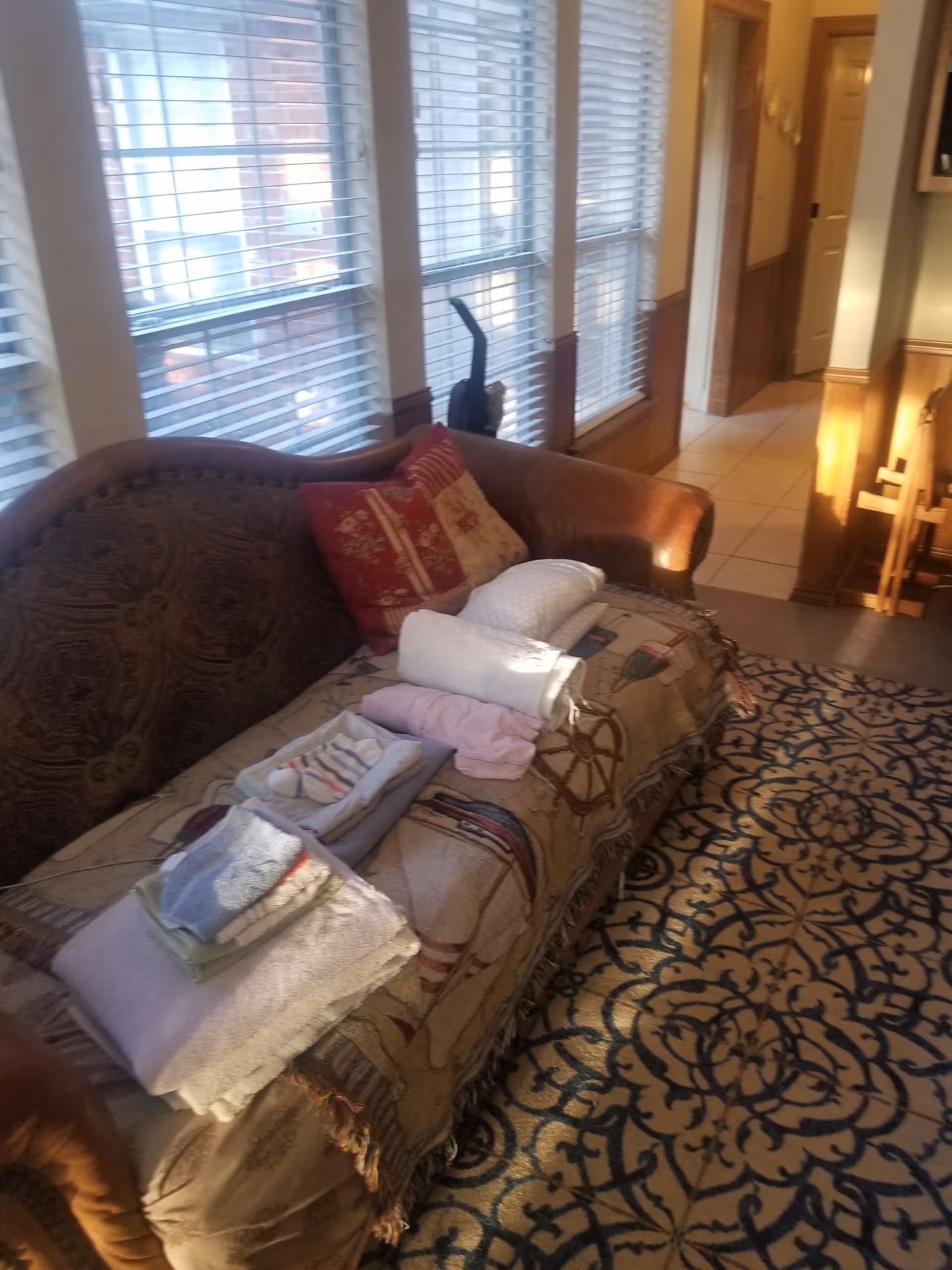 Cozy living room with a sofa, folded towels, and large windows along the wall.