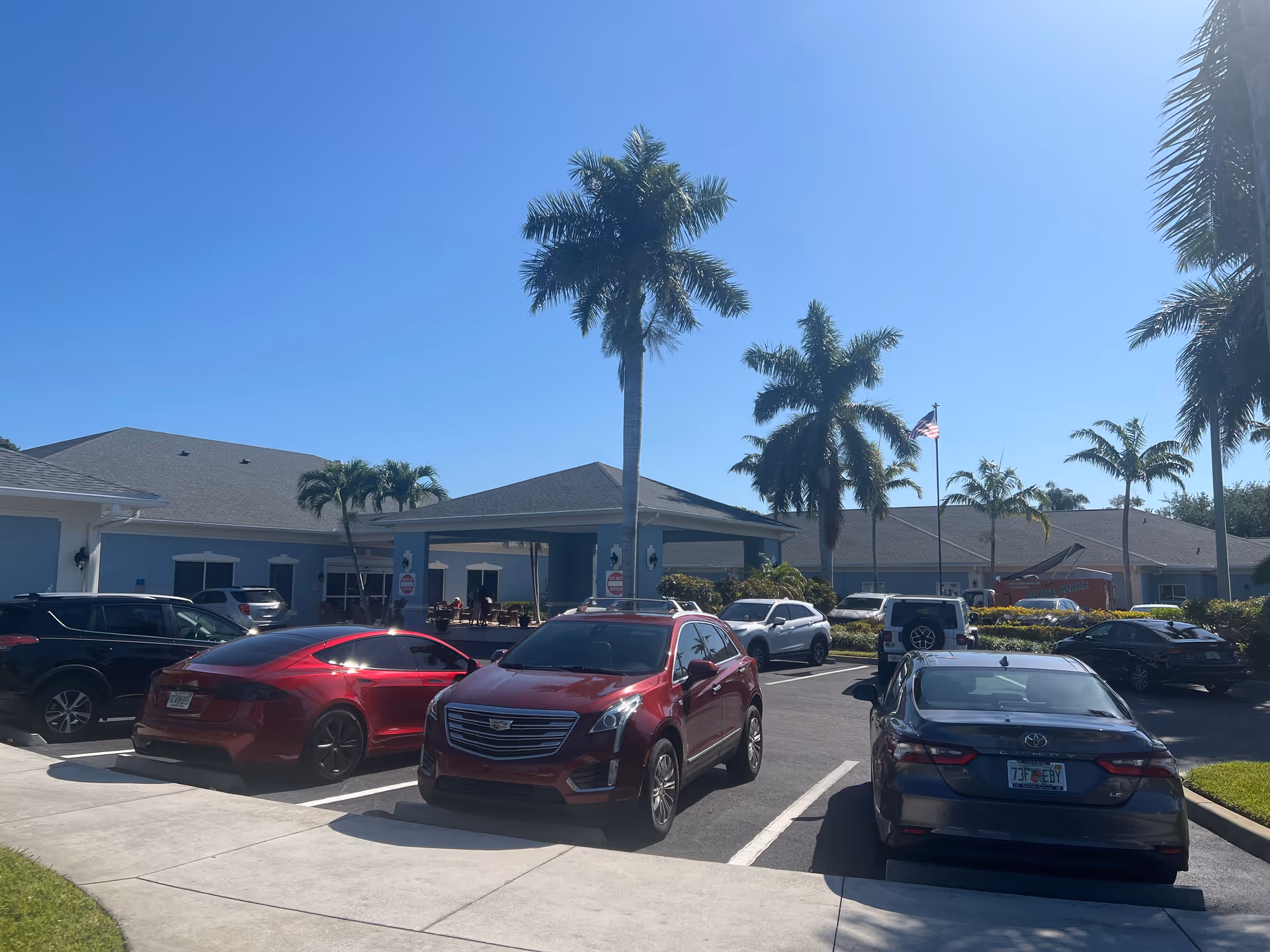 Blue-sky day at Lynmore at Lawnwood, with a blue facility front, palm trees, and parked cars.