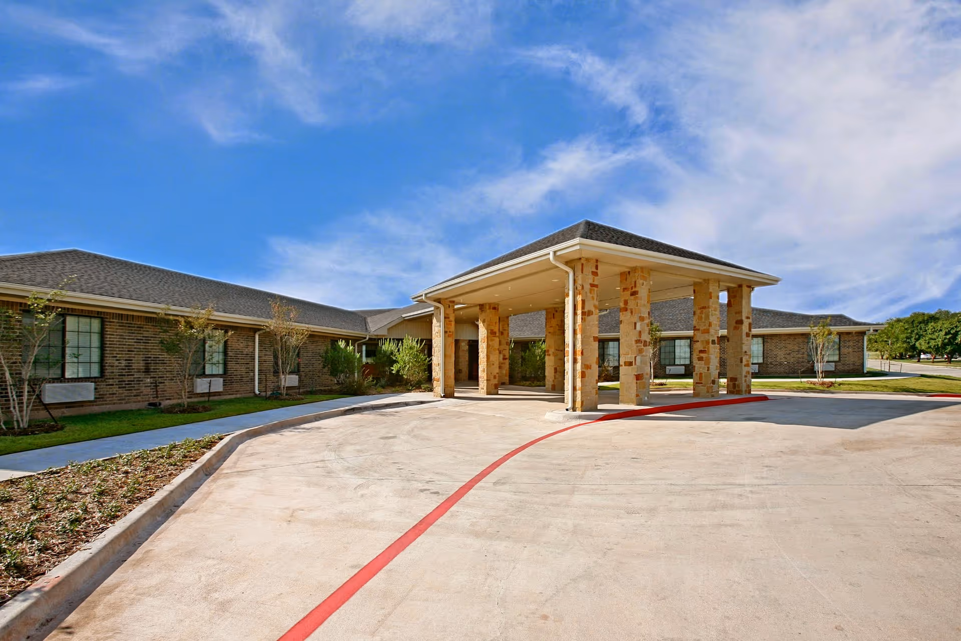 Senior living facility exterior with brick building, porte-cochere entrance, and curved driveway.