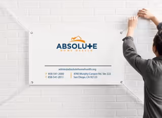 Person hangs a sign for Absolute Home Health on a white brick wall.