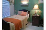 An adjustable hospital-style bed in a cozy senior living center bedroom with nightstand and lamp.
