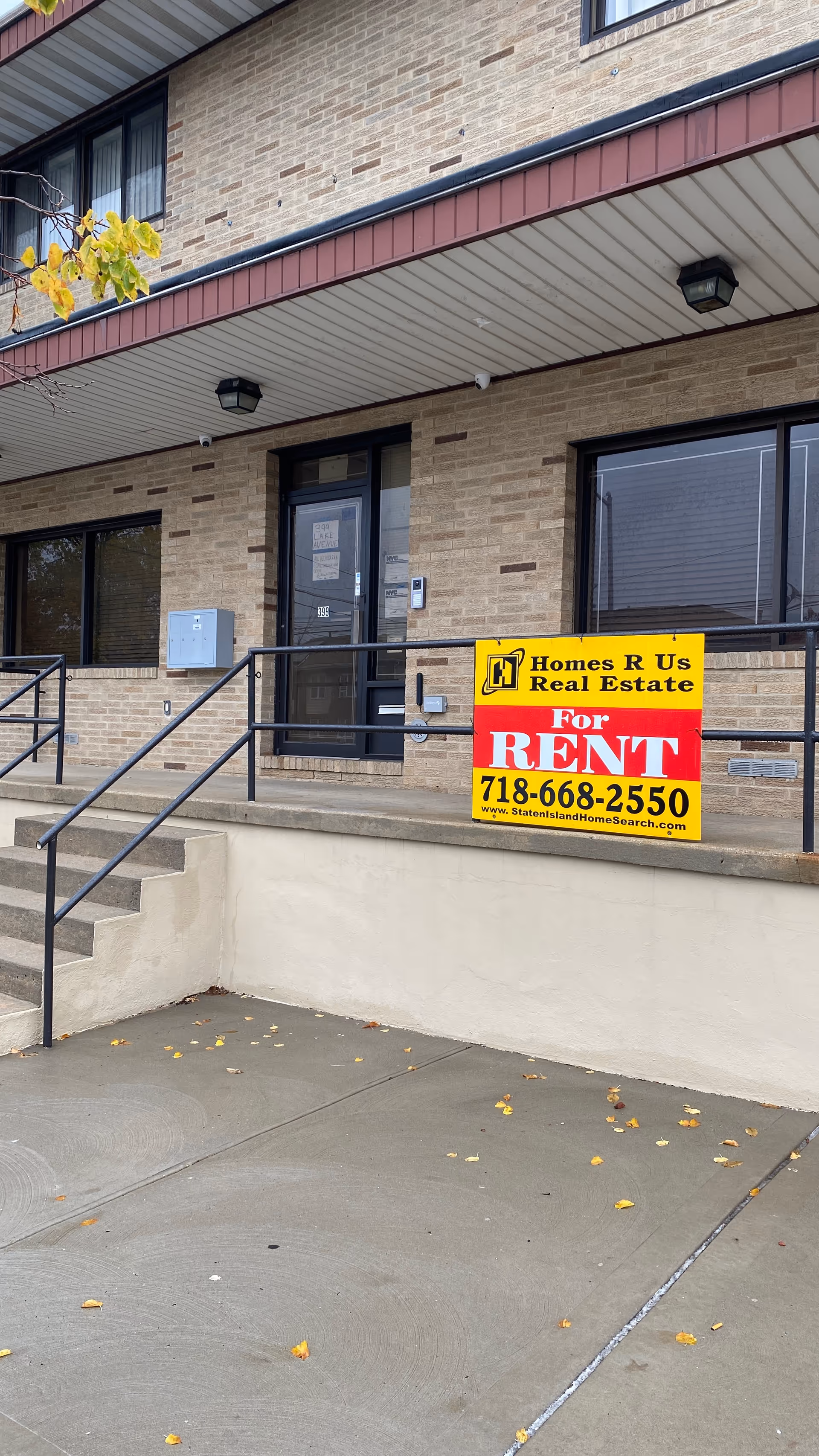 Brick building entrance with stairs and a prominent yellow For Rent sign.