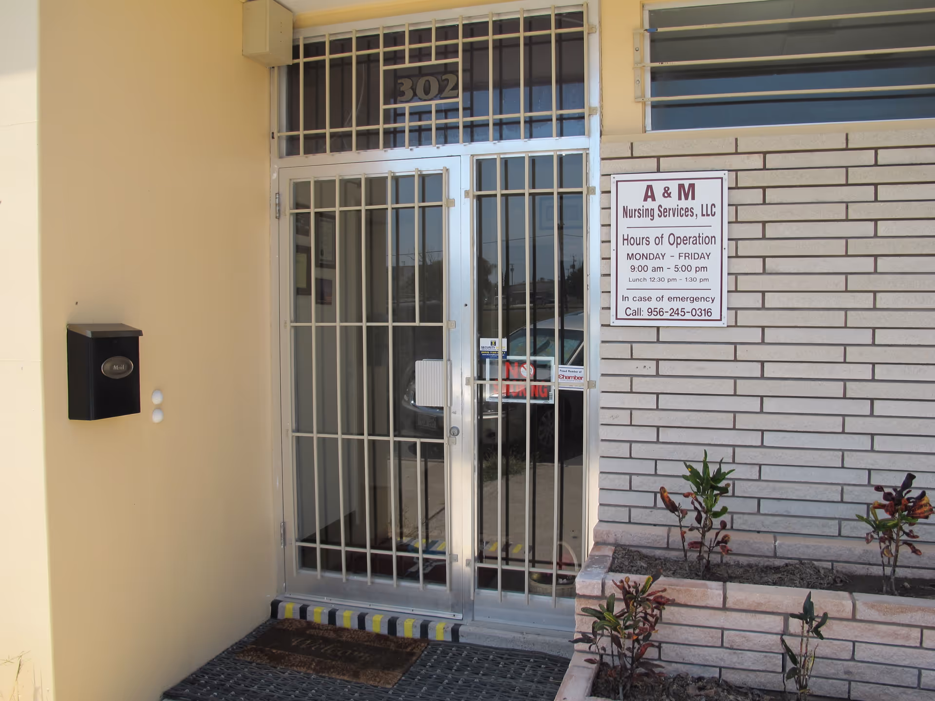 Metal barred glass door entrance of A & M Nursing Services, LLC, with sign and landscaping.