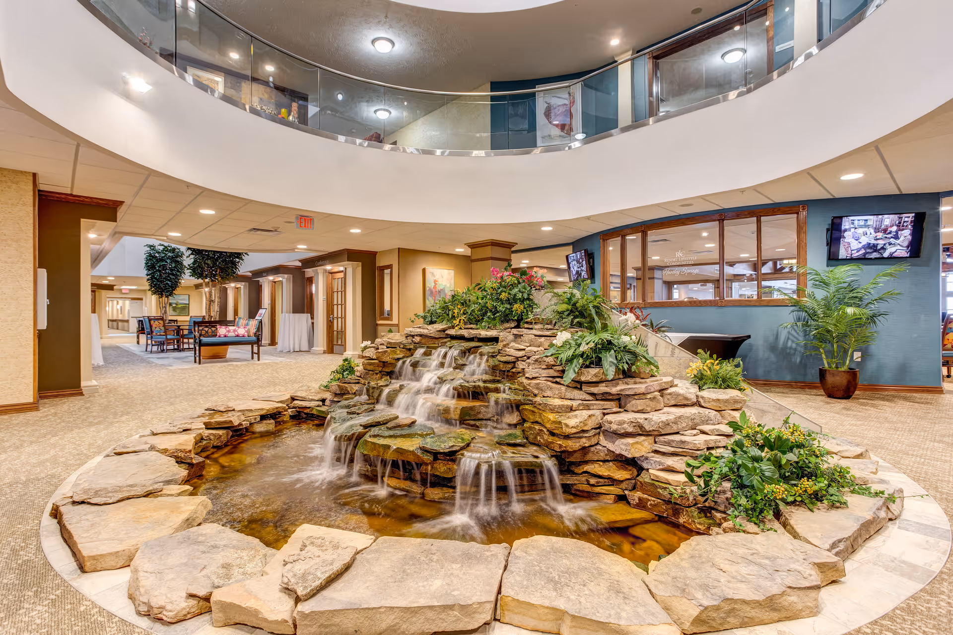 Interior atrium with a layered rock fountain, plants, and seating in Seaside Springs Retirement Community.