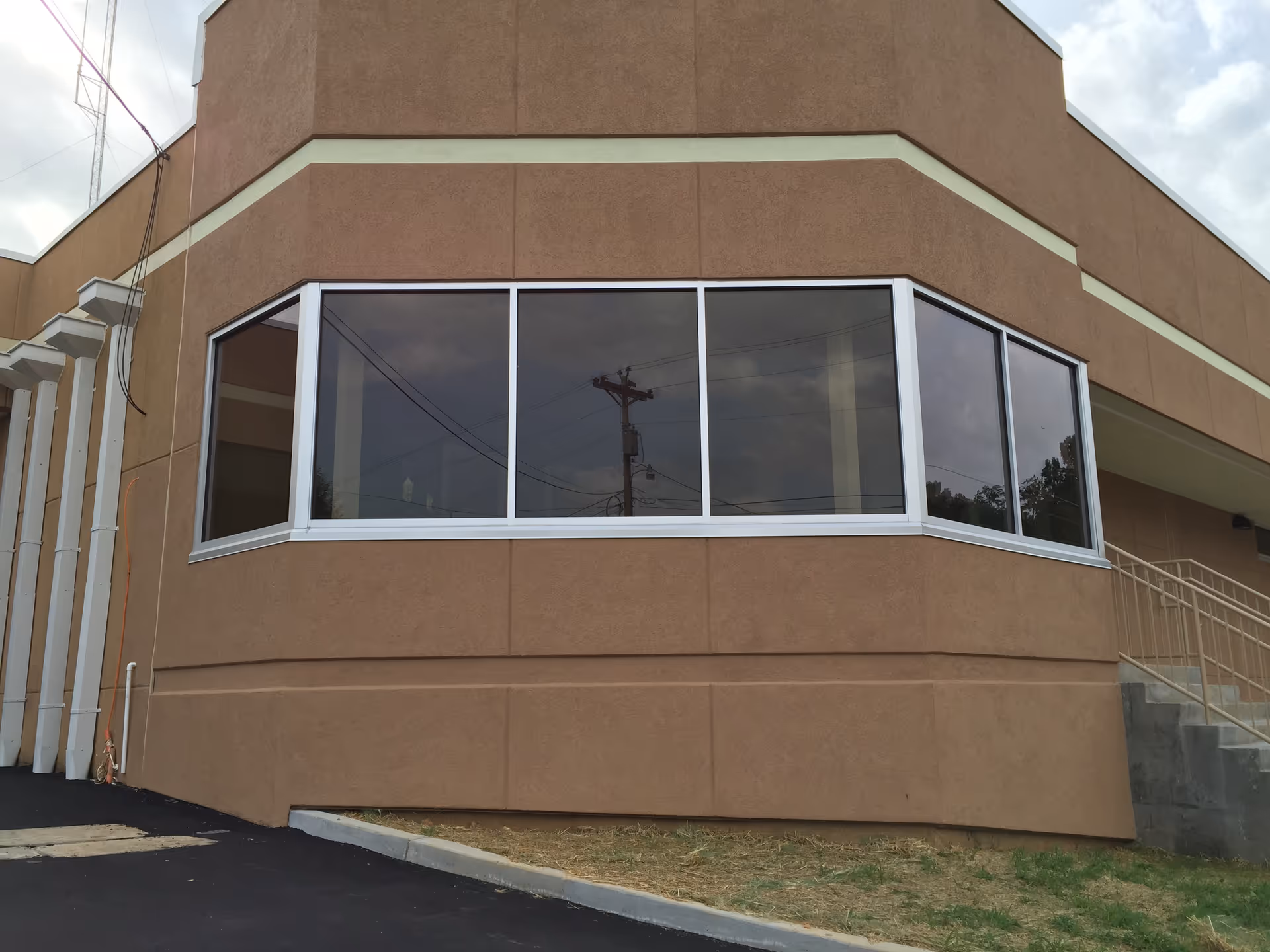 Front view of a brown stucco building with large corner windows and a right-side stairway.