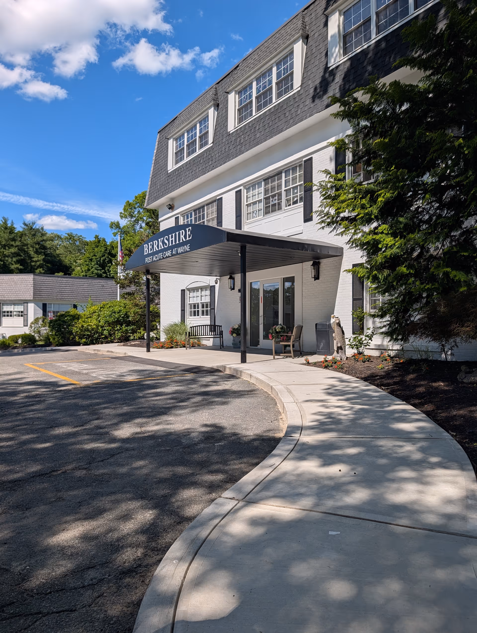 Exterior view of a senior care facility entrance with a curved sidewalk and porch seating.