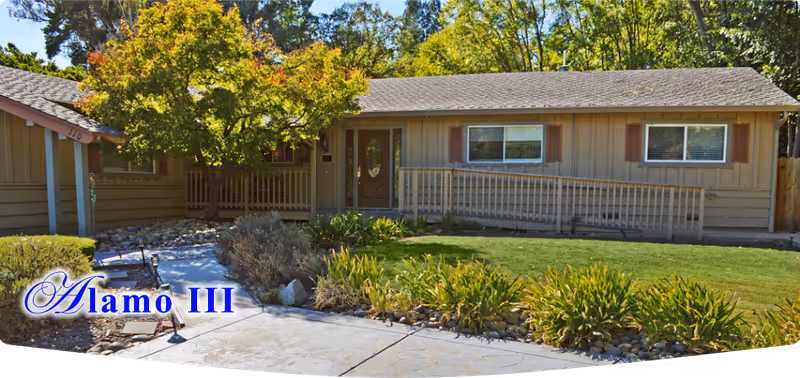 Single-story senior residence with ramped entrance, landscaped front yard, and 'Alamo III' text.