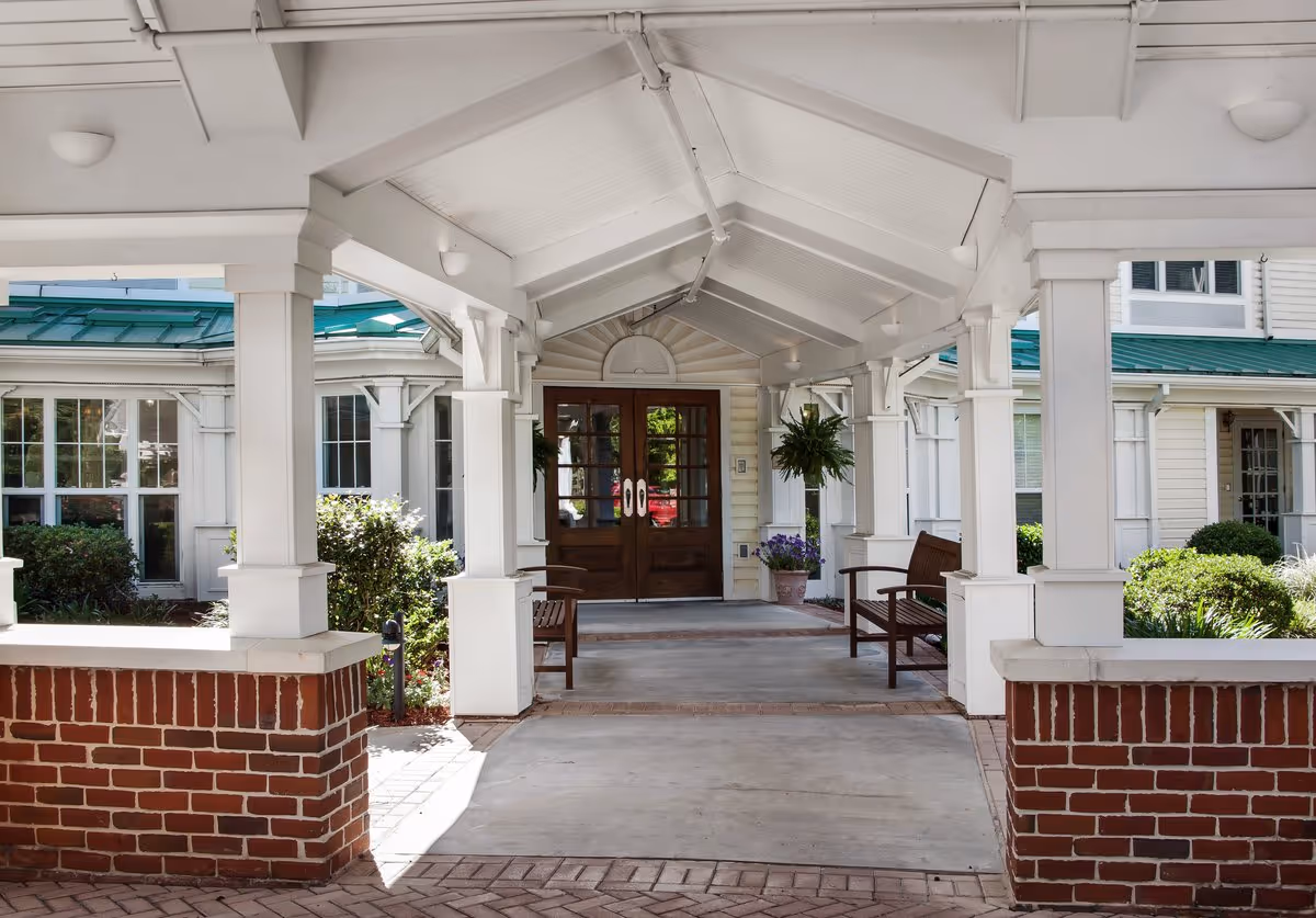 Covered entrance with white columns, benches, hanging plants, and double wooden doors leading into the building.