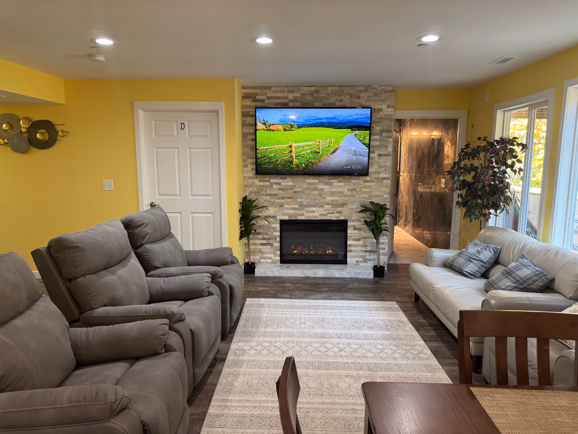Bright yellow living room with stone fireplace, wall-mounted TV, and beige seating.