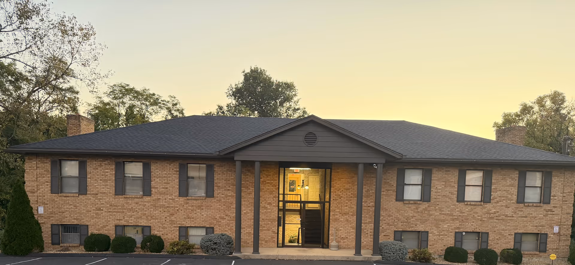 A brick senior living facility exterior with a central entrance and shrubs.