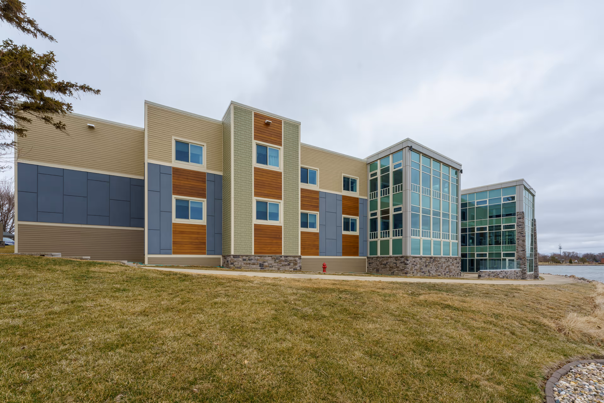 Modern multi-section senior living facility exterior with glass entry, stone accents, and a grassy lawn.