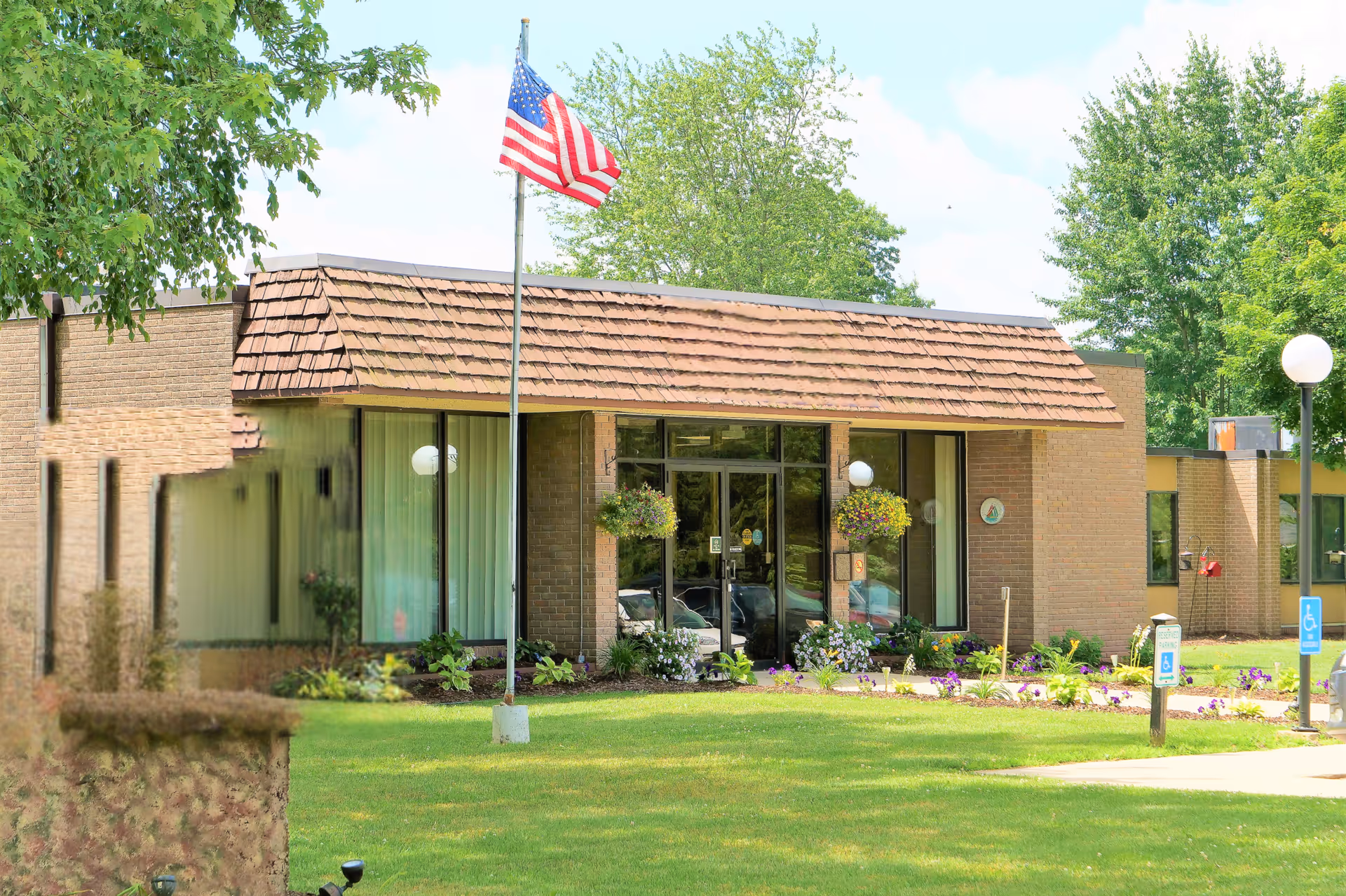 Metron of Cedar Springs exterior entrance with flag, glass doors, and manicured landscaping.