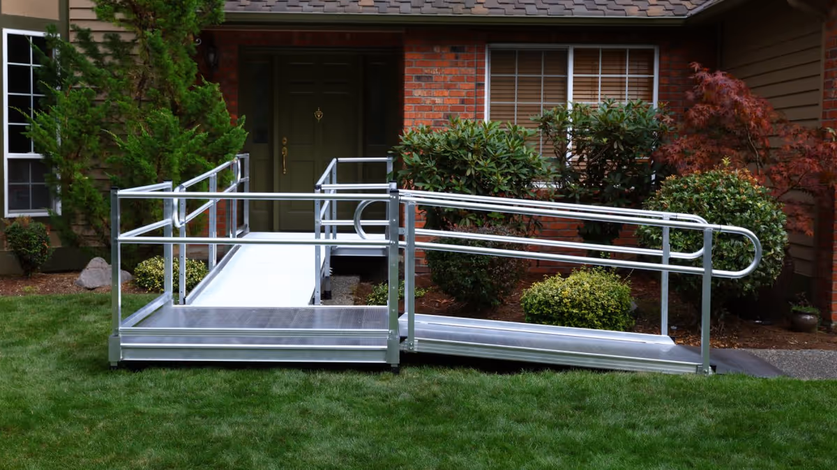 Metal wheelchair ramp leads to a brick building entrance amid greenery.