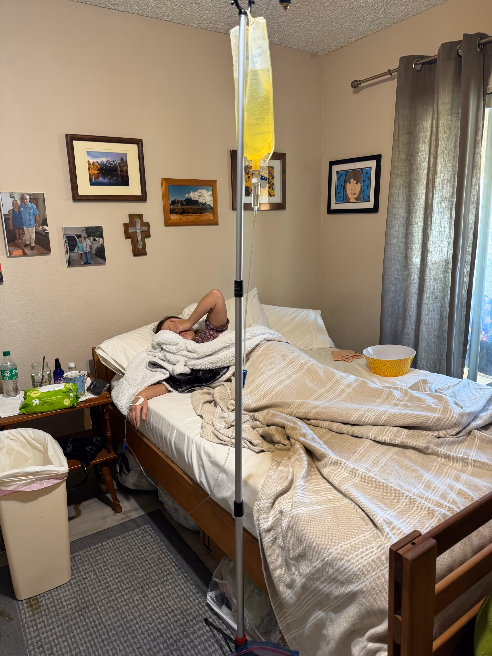 Resident lies in bed connected to IV drip in a decorated bedroom with curtains.