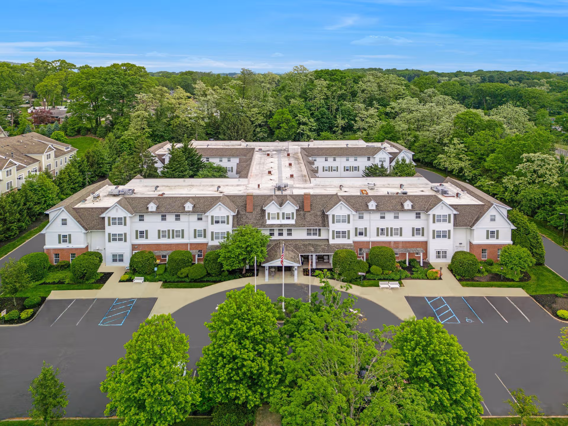 Aerial view of Brighton Gardens of Mountainside's white, multi-wing building with parking and trees.