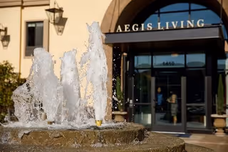 Stone fountain spraying water in front of the Aegis Living Ravenna entrance.