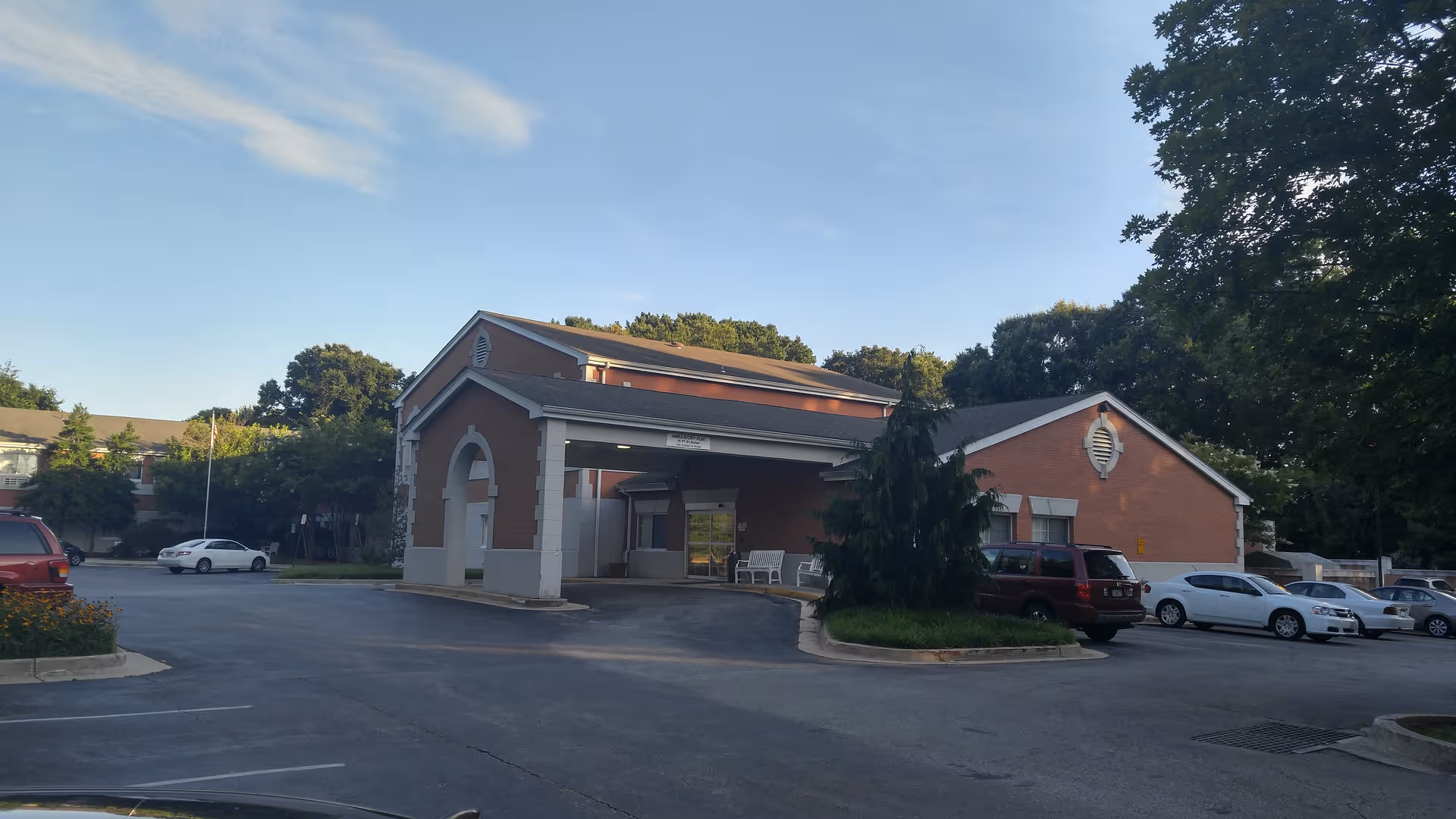 Exterior view of a brick senior living facility with a covered entrance and parking.