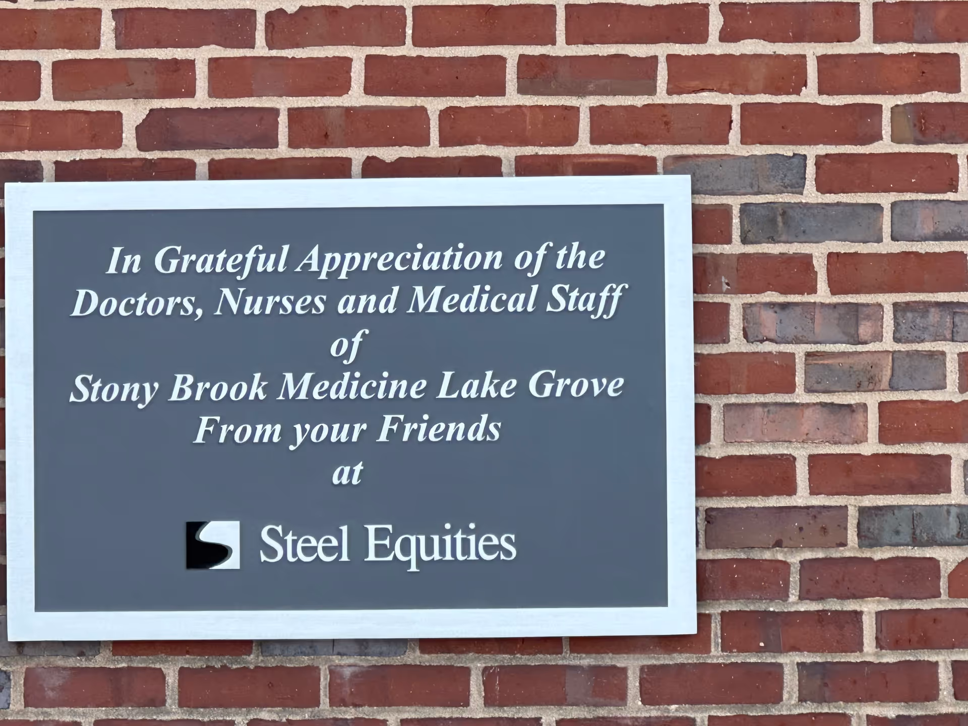 A gray plaque mounted on a red brick exterior wall.