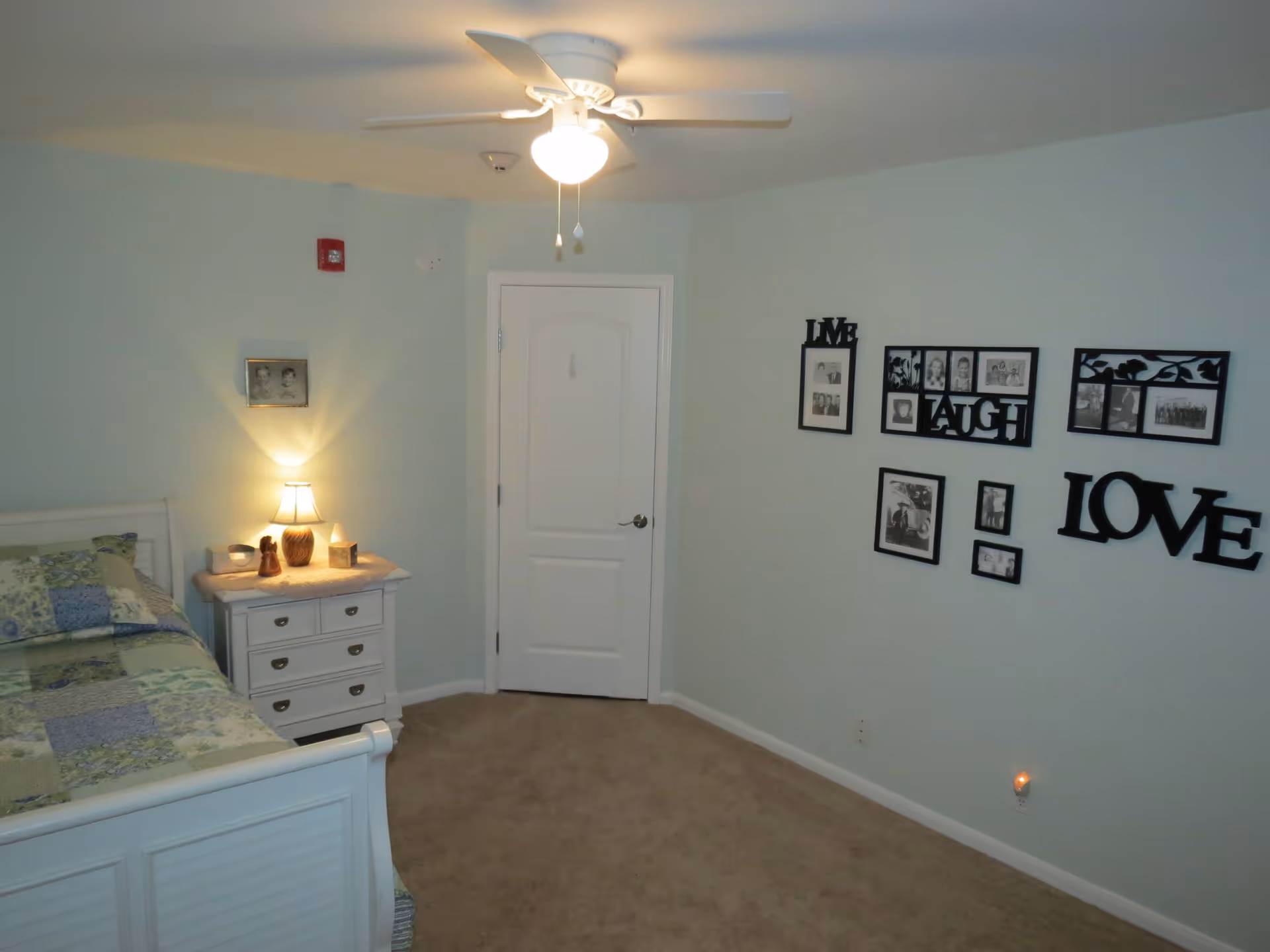 Bedroom with a bed, nightstand and lamp, ceiling fan, and framed photo wall art spelling "LOVE".