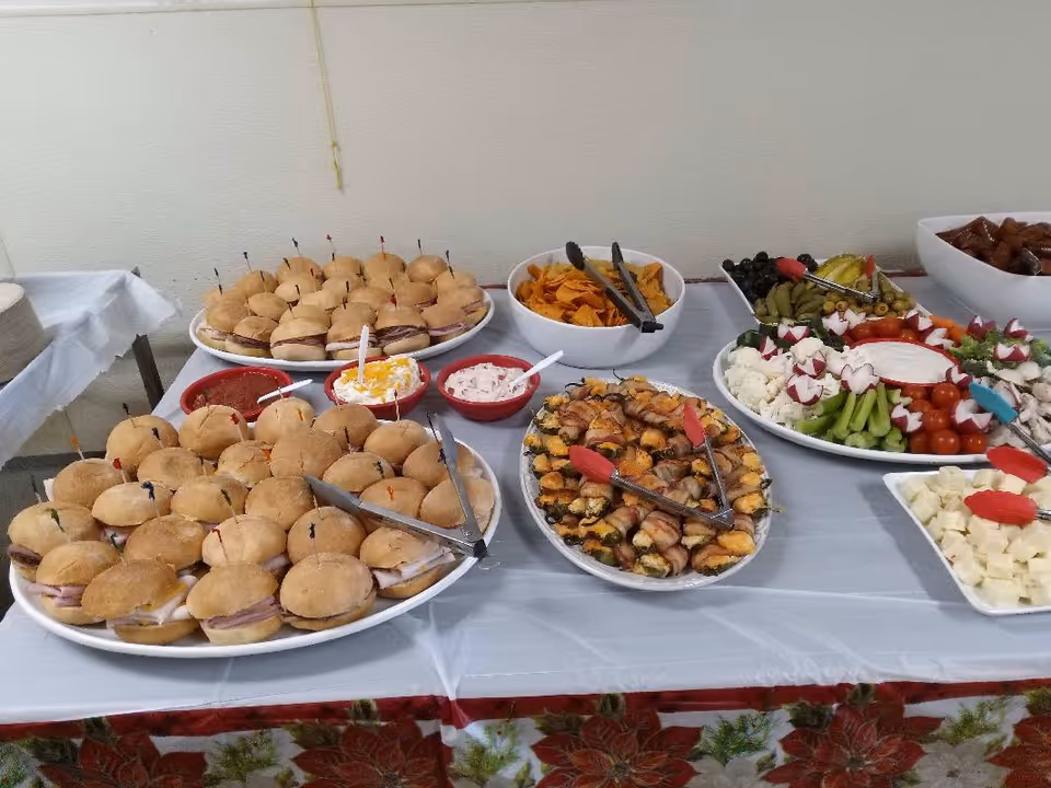 Indoor buffet table with sliders, chips, fruit, vegetables, and dips arranged for a community event.