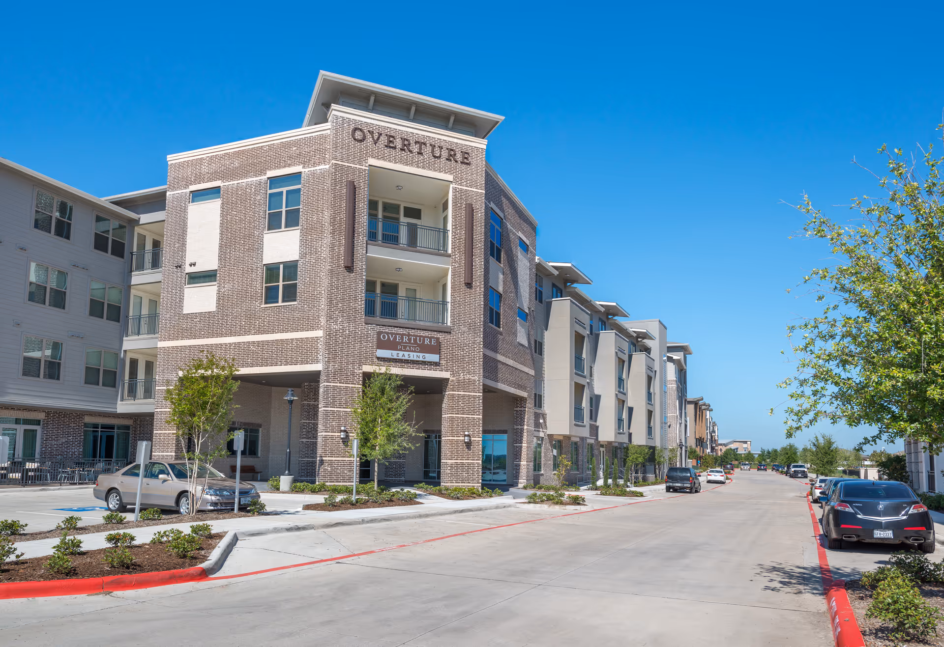 Exterior view of Overture Plano senior living complex with parked cars.