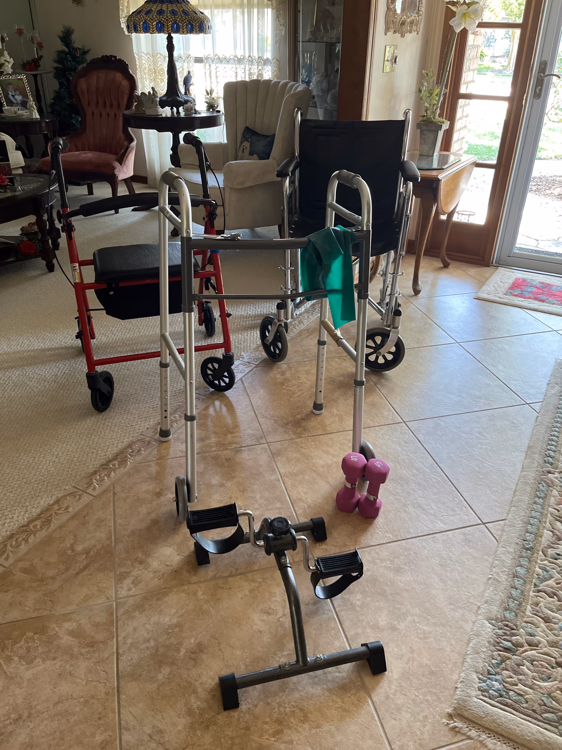 Indoor living area with walkers, a pedal exerciser, dumbbells, and chairs.