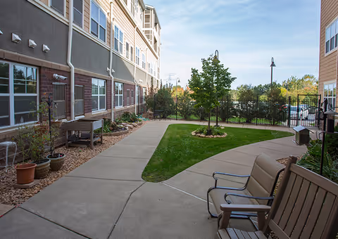 Exterior view of Ecumen Seasons at Maplewood outdoor courtyard with benches, walkway, lawn, and trees.