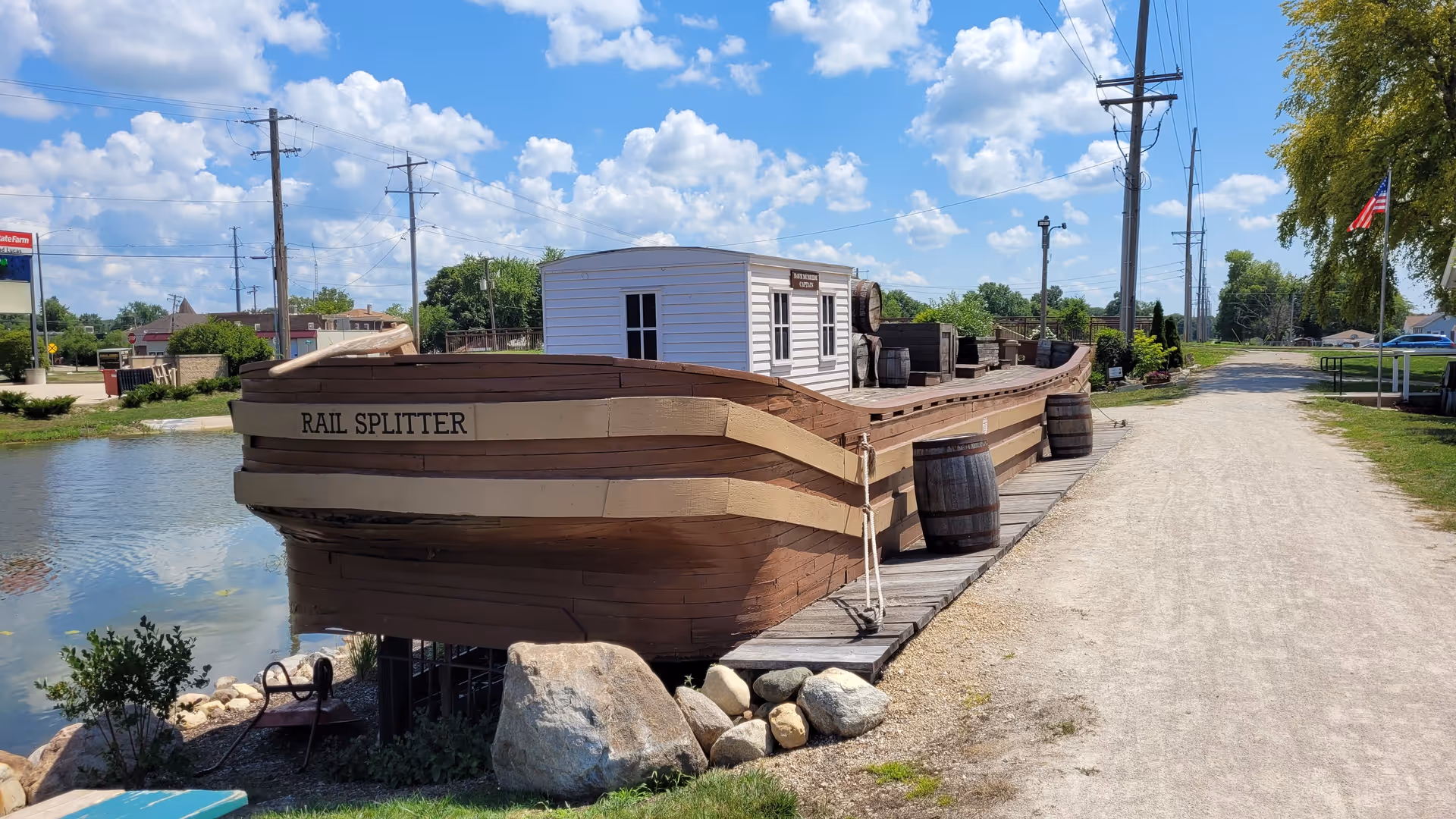 A brown wooden boat named Rail Splitter sits dockside beside a gravel path and water.