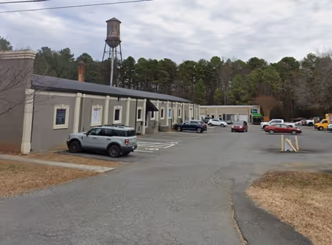 Exterior view of a senior living facility with a parking lot and trees behind.
