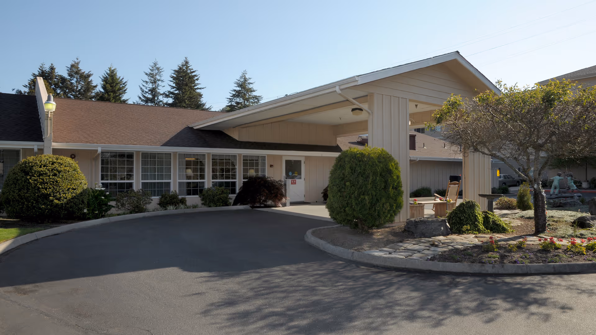 Exterior view of a single-story senior living facility with a covered entrance and curved driveway.
