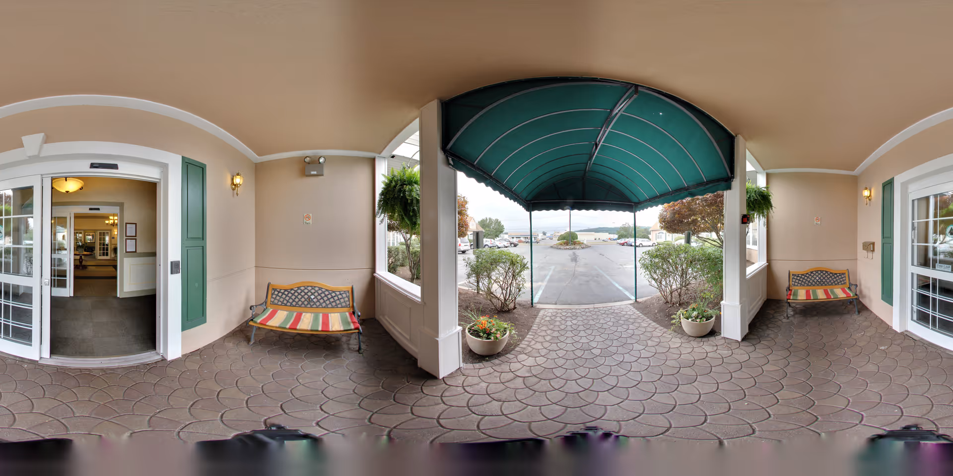 Covered front entrance with a green awning, two benches, potted plants, and glass double doors leading into the facility.